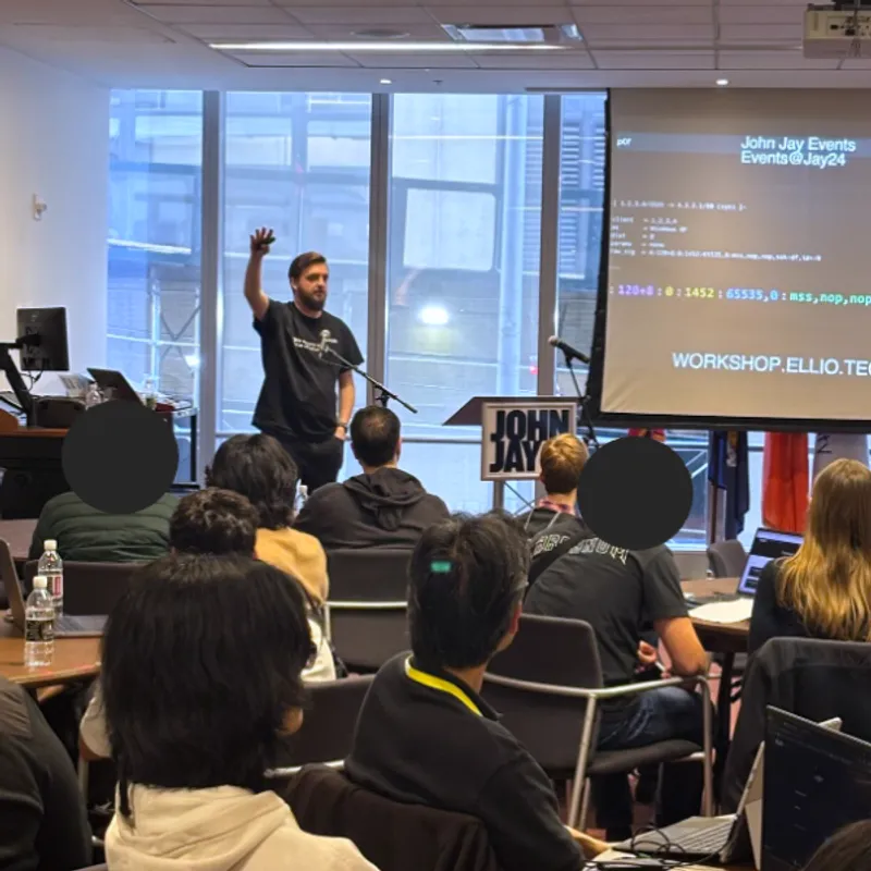 Vlad Iliushin presenting at cybersecurity workshop with audience seated in conference room, projection screen showing "WORKSHOP.ELLIO.TECH" and technical data