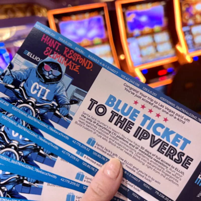 Hand holding ELLIO cybersecurity  materials including "Blue Ticket to the IP Verse" with threat intelligence data sheets in front of illuminated display screens