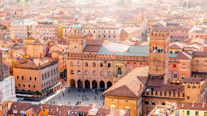 Aerial view of historic Italian city center in Bologna with medieval architecture, red-tiled roofs, and central piazza surrounded by traditional buildings